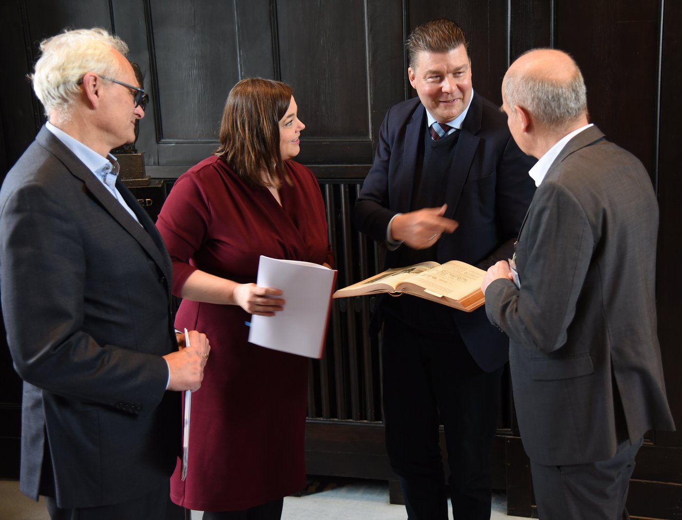 The picture shows from left to right Martin Görge, Katharina Fegebank, Andreas Dressel and Jürgen May. They are bending over a historical book about the BNITM from 1914.