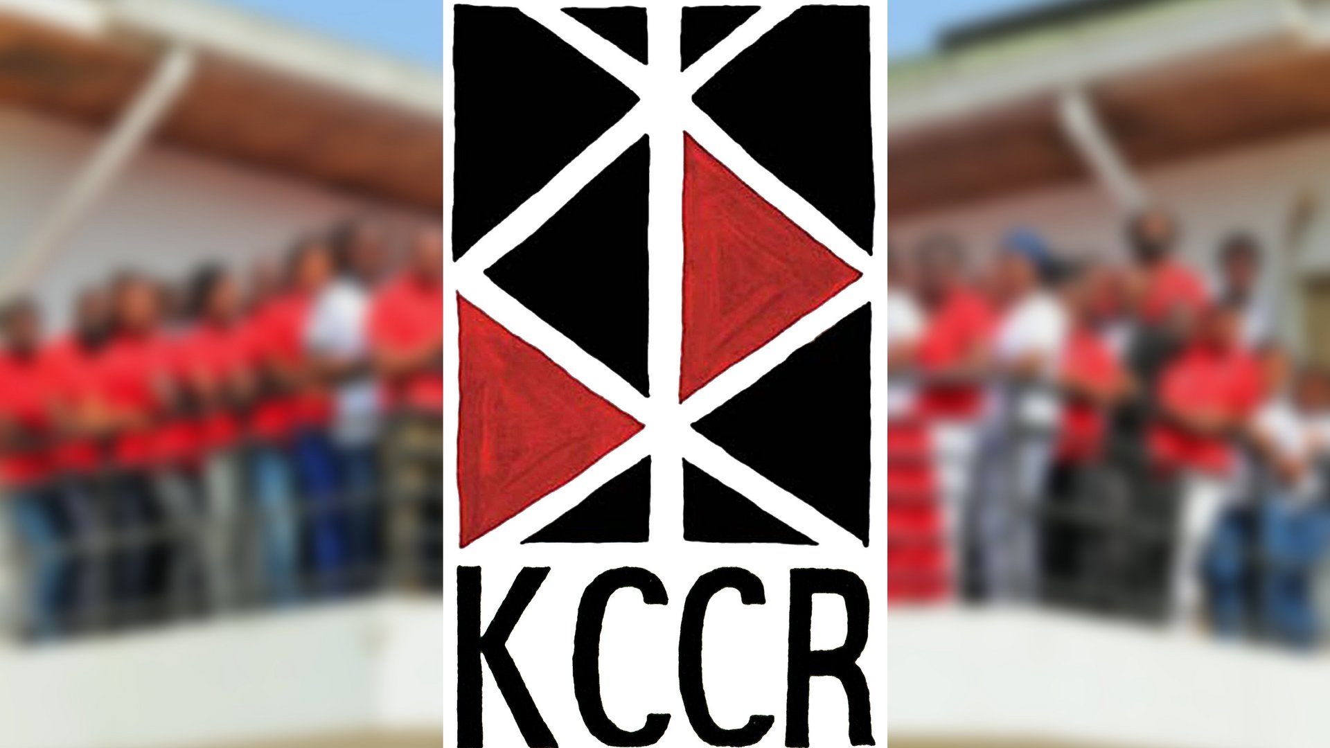 The picture shows the red and black logo of the KCCR, with the Institute's staff blurred behind it on the Institute's balcony.
