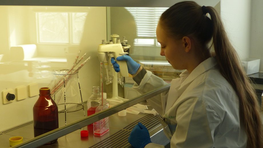 Das Foto zeigt eine Jugendliche im weißen Laborkittel beim Pipettieren an einer Lab Bench.